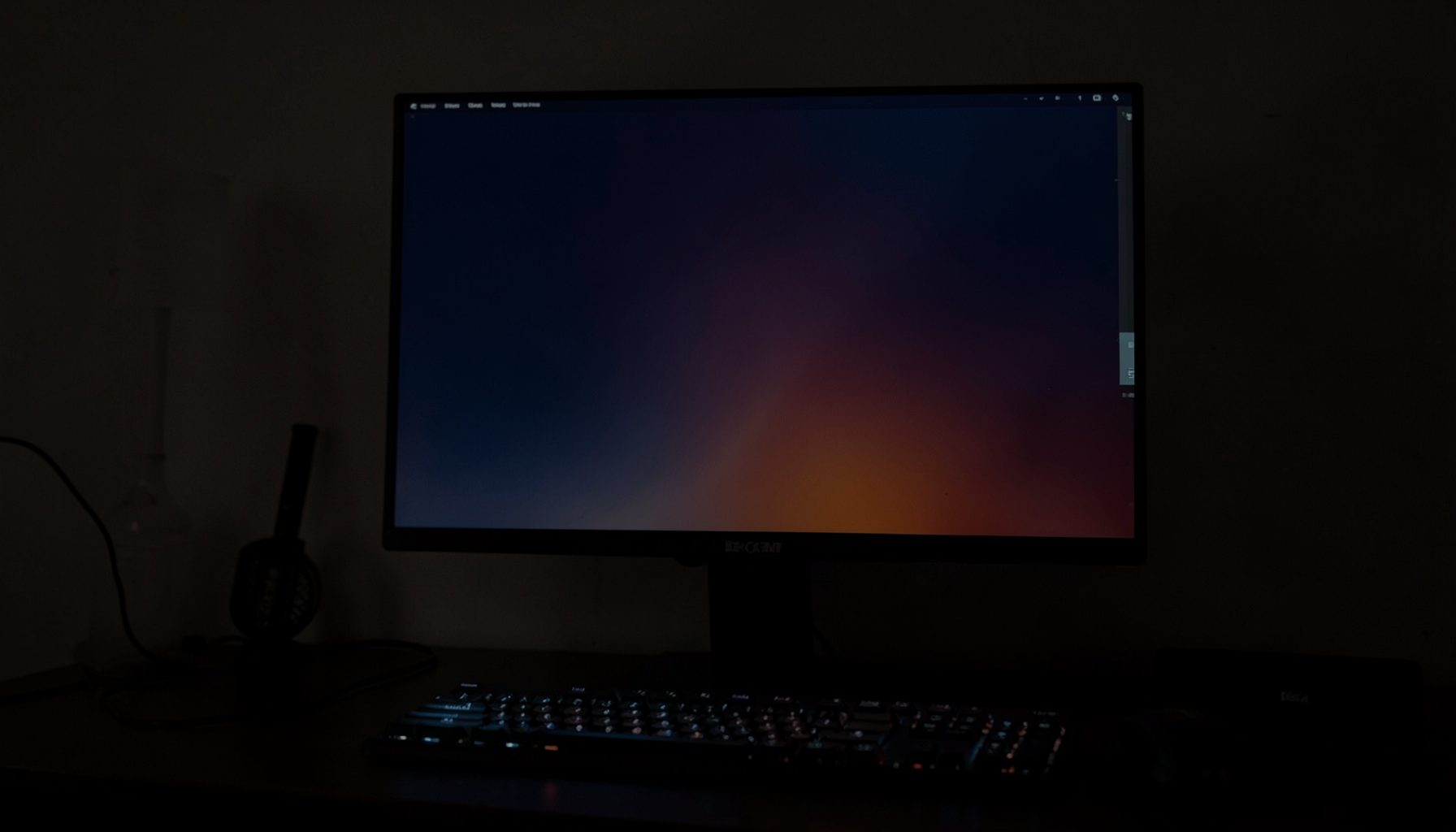 A dark atmospheric desktop setup with a glowing monitor displaying an abstract gradient wallpaper in deep navy and orange