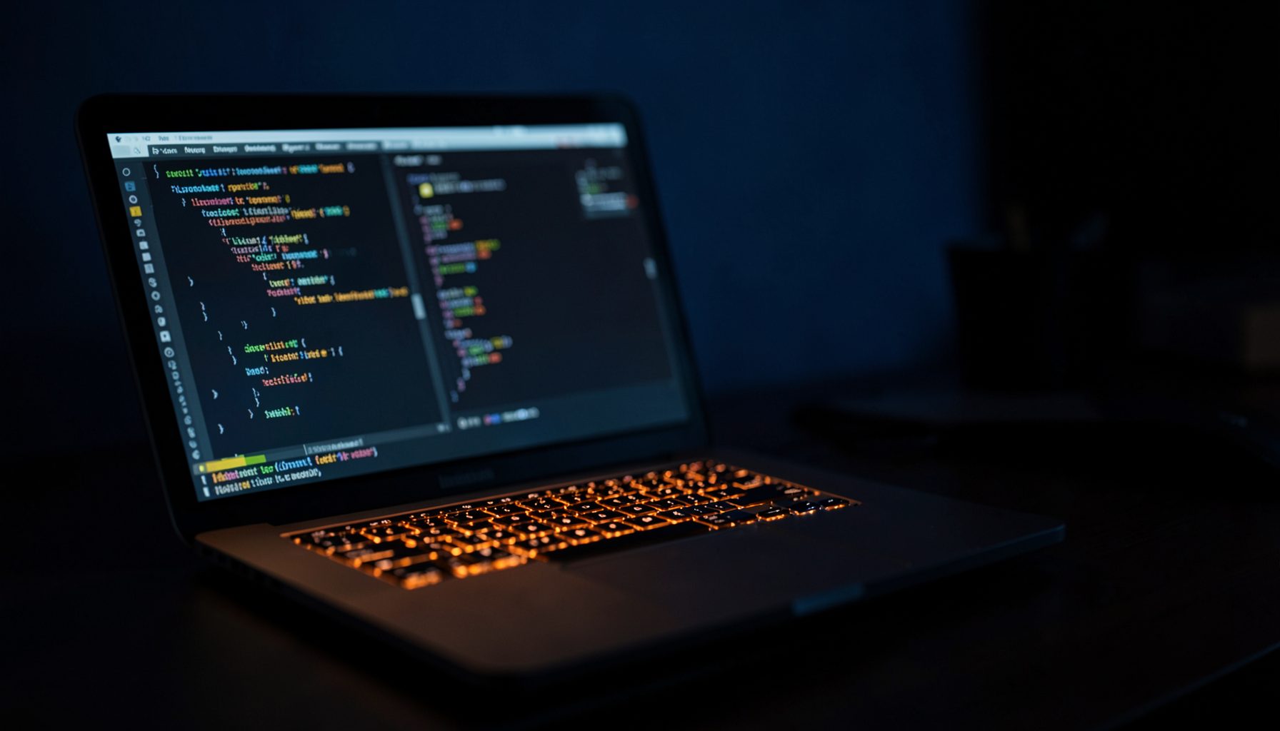 A dark desk setup with a glowing laptop screen displaying code and interface panels, warm orange accent light spilling across the surface