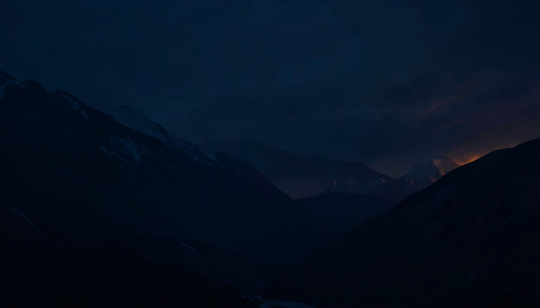 A moody desktop wallpaper featuring a dark abstract landscape with navy blue and subtle orange highlights